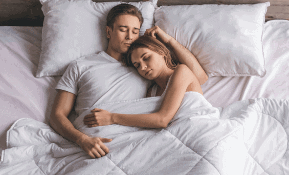 A couple lying in bed in the proper cuddling position to display body language.
