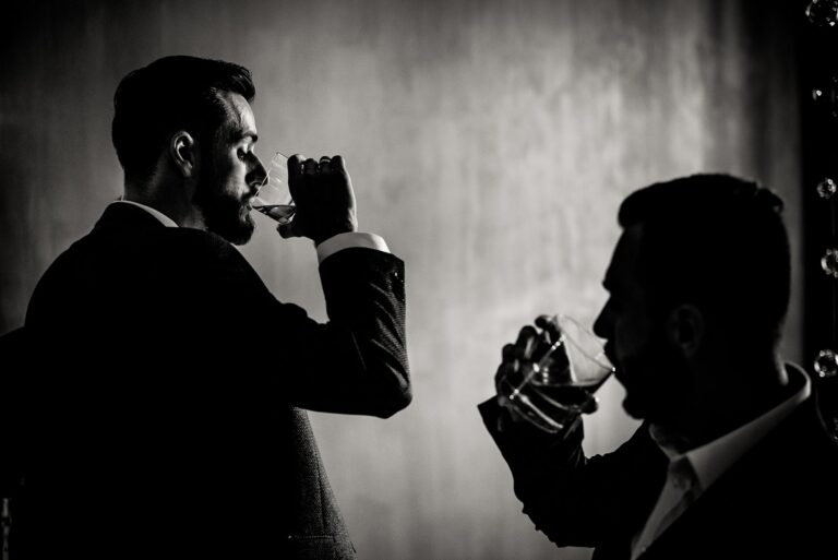 Monochrome view of two men who are drinking alcohol drinks indoo